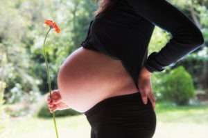 Schwangere Frau hält eine Blume in der Hand